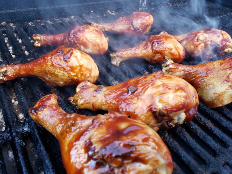 Grill drumsticks on the barbecue grill, several chicken drumsticks cooking on the grill grates.