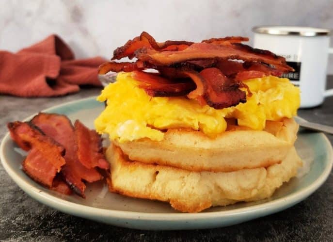 11 Savory and Sweet Waffle Toppings, Bacon, egg, and cheese stacked on two waffles with a side of bacon