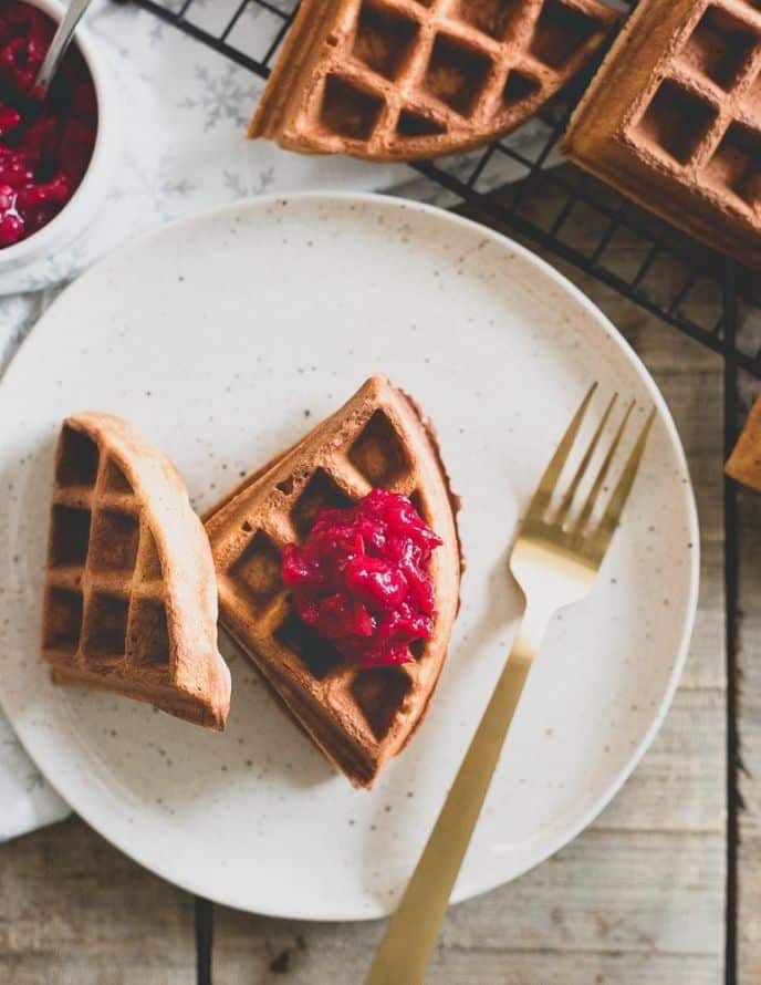 Waffles topped with a red colored vanilla cranberry compote on a white plate