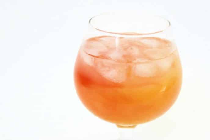 Lemonade cocktail recipe made with juices, in a glass with ice, white background