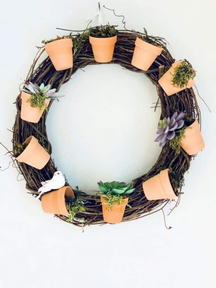 Completed succulent wreath with terracotta clay pots, moss, succulents, and a fake bird perched on a pot.